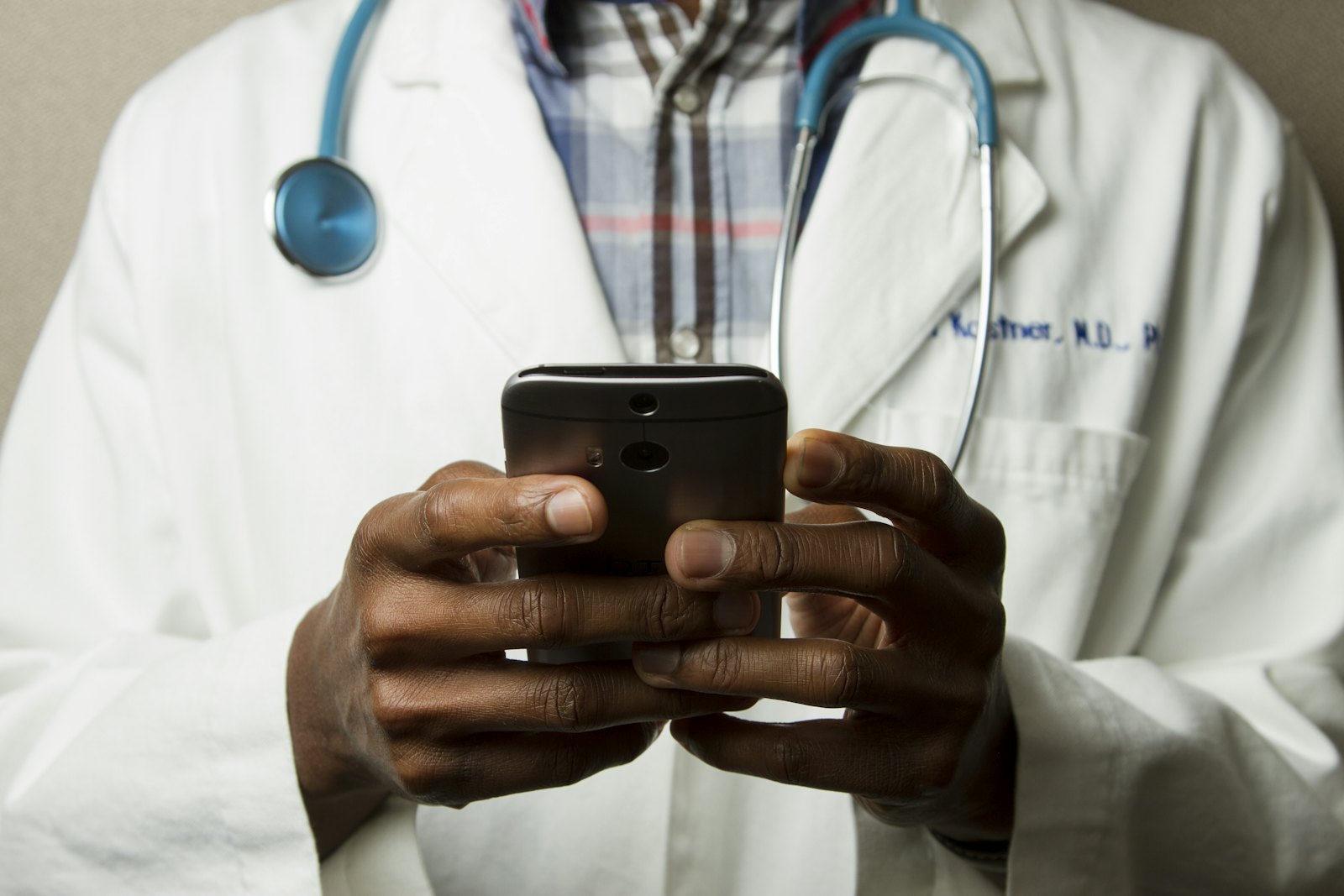 A doctor in a white coat with a stethoscope using a smartphone